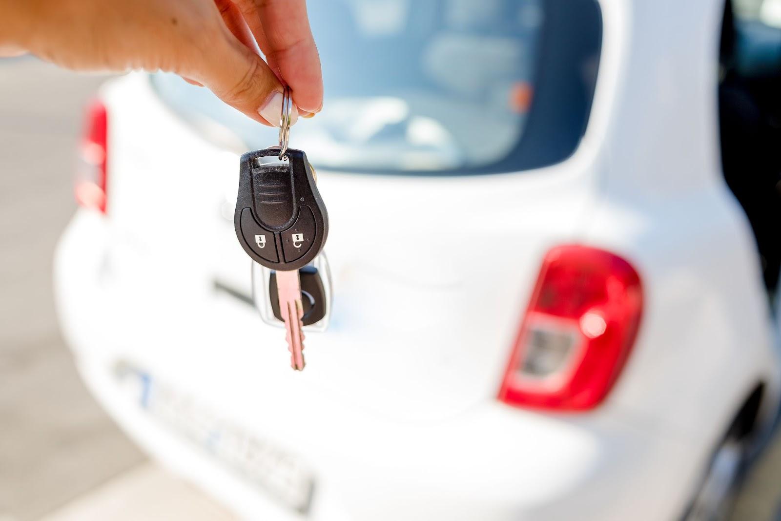 A hand holding car keys with a white car in the background, symbolizing the flexibility of long-term car rentals