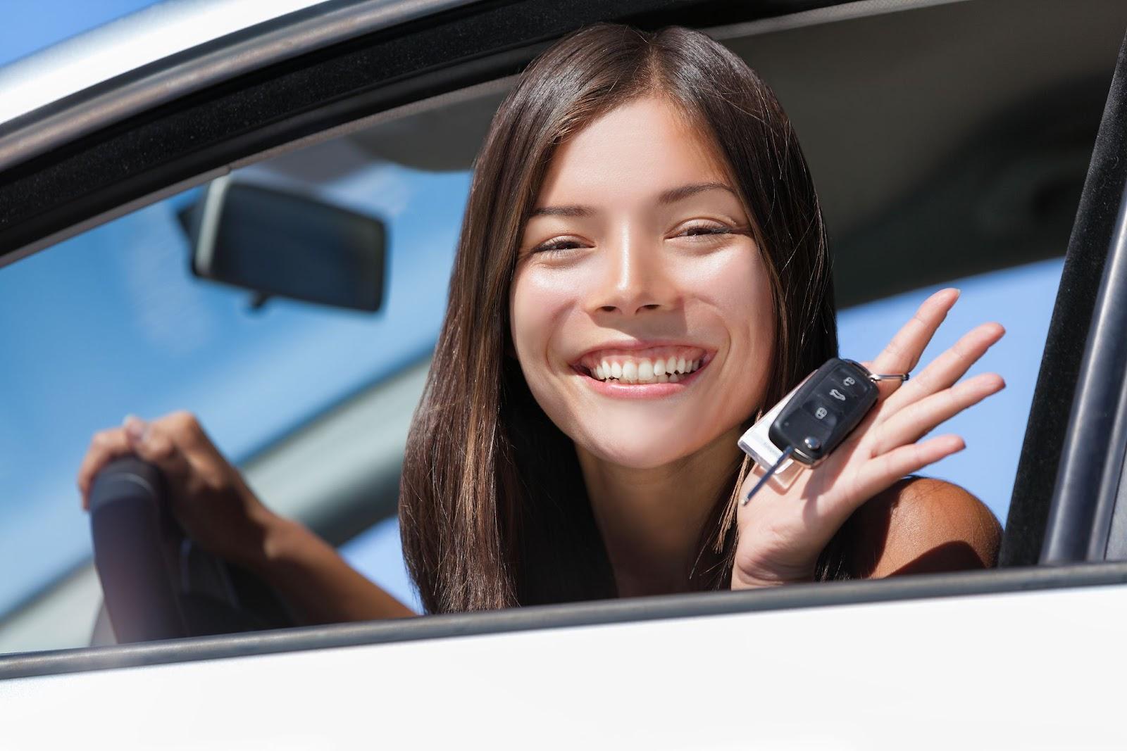 A young woman smiling in her car, holding keys, representing the joy and convenience of using long-term car rental services